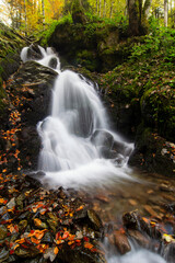 Fototapeta na wymiar Waterfall flowing through rocks in a deep forest, autumn landscape