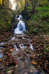 Waterfall flowing through rocks in a deep forest, autumn landscape - 542437471