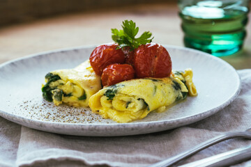 Omelet with spinach and roasted cherry tomatoes on wooden table, healthy breakfast