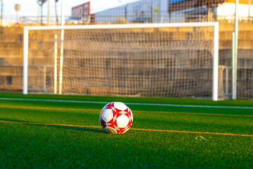 Soccer ball on the grass in front of the field. View from the ground of a soccer ball in front of the field. View of a soccer ball on the grass with a field in the background