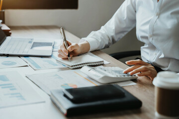 Women businessman hand using calculator and writing make note with calculate about cost at home office.