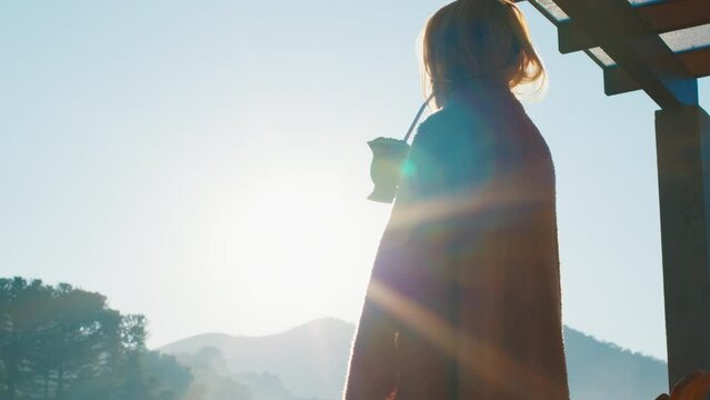Woman drinks mate tea and enjoys sunrise in Brazilian mountains from the wooden terrace