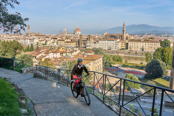 cheerful senior woman cycling with her electric mountain bike above  downtown of Florence  with...