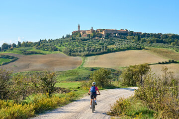 nice senior woman riding her electric mountain bike  in the Ghianti area beow the skyline of the medieval city of Pienza , Tuscany , Italy - obrazy, fototapety, plakaty