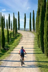 Fotobehang nice senior woman riding her electric mountain bike in a cypress avenue in the Chianti area near Pienza, Tuscany , Italy © Uwe