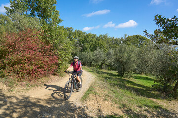 Fototapeta na wymiar nice senior woman riding her electric mountain bike between olive trees in the Casentno hills near Arezzo,Tuscany , Italy