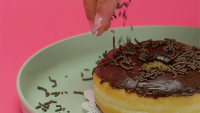 Chocolate being sprinkled on a donut by a women chef