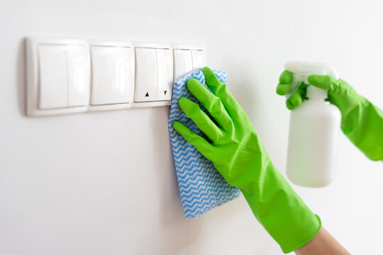 Person In Gloves Cleaning Light Switch With Spray And Rag