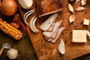 still life of food in a rural style on a dark wood background, sliced lard and garlic, cheese, corn...