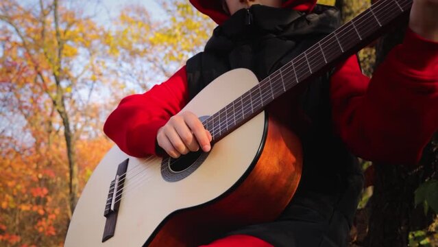 against the backdrop of an autumn forest, a close-up of a guitar that a boy holds and plays a melody. High quality FullHD footage
