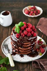 Chocolate Pancakes. Pancakes with fresh raspberry with chocolate glaze or toppings in gray bowl on old wooden table background. Homemade classic american pancakes. Page for magazine concept.