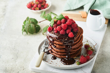 Chocolate Pancakes. Pancakes with fresh raspberry with chocolate glaze or toppings in gray bowl on light gray table background. Homemade classic american pancakes. Page for magazine concept.