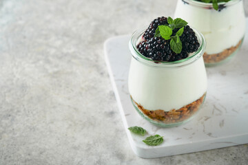 Yogurt with granola, blackberry berry fruits and muesli served in glass jar on gray concrete table background. Healthy breakfast concept. Healthy food for breakfast, top view