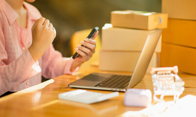 Start SME, small business entrepreneurs, SMEs of freelancers. Close-up shot of an Asian woman using a smart phone and laptop with box. Her Asian woman raises her hand. Online Marketing Packaging Box a