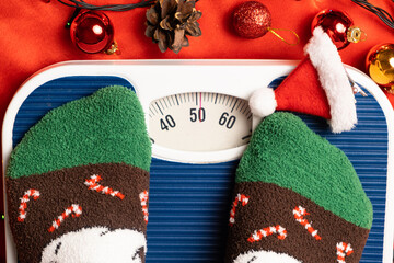 A woman in Christmas socks stands on the scales, weighs herself after gluttony during the holidays