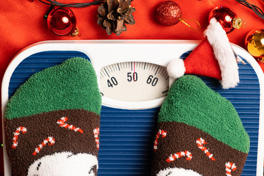 A woman in Christmas socks stands on the scales, weighs herself after gluttony during the holidays