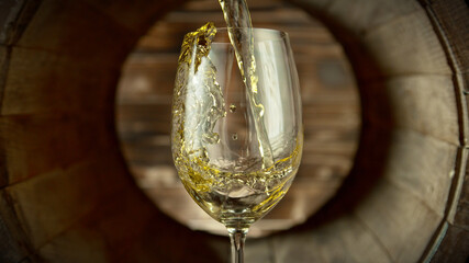 Pouring white wine into glass inside old wooden barrel.