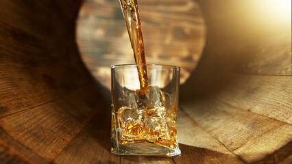 Pouring whisky into glass inside old wooden barrel.