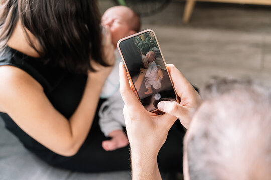 Father taking photo of baby with cell phone while baby eats - Powered by Adobe