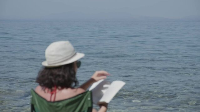 What stories will this summer bring? Beautiful woman reading on beach. Blurred effect