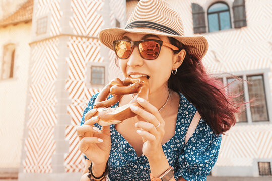 Happy girl tourist eating traditional pretzel snack on the background of the Ledenhof building in Osnabruck, Germany