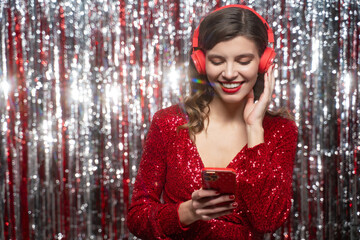 Silent disco, music lover in red festive dress listening to favorite song in headphones using phone