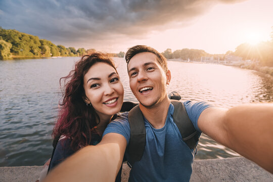 A couple in love or just friends students takes a selfie photo with scenic sunset lake view in city park. Vacation, education and relationship concept - Powered by Adobe