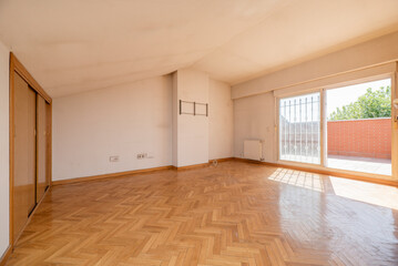 Fototapeta na wymiar Empty living room with fitted wardrobes, parquet floors, sloping ceilings and access to a terrace with a fence