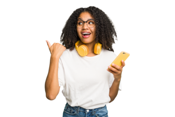 Young african american woman listening to music with yellow headphones isolated points with thumb finger away, laughing and carefree.