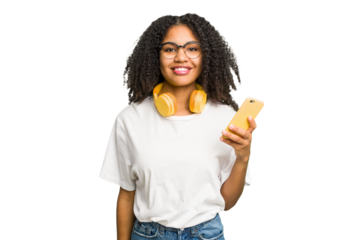 Young african american woman listening to music with yellow headphones isolated happy, smiling and cheerful.