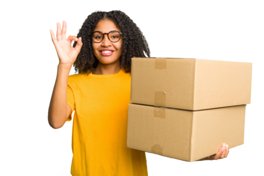 Young african american woman moving to other house while picking up a box full of things isolated cheerful and confident showing ok gesture.