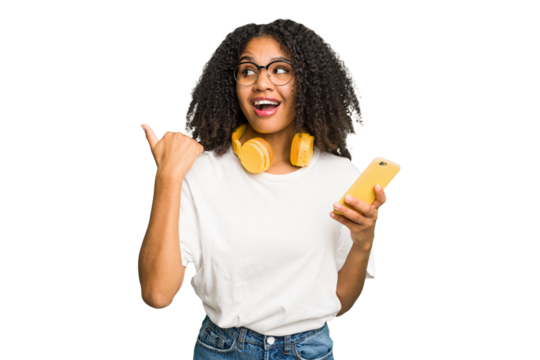 Young african american woman listening to music with yellow headphones isolated points with thumb finger away, laughing and carefree.