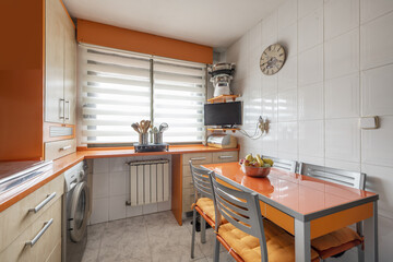 Corner of a conventional kitchen with bright orange cabinets combined with beech wood and a rectangular table with matching chairs