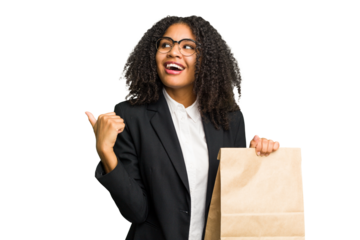 Young african american business woman holding a take away bag isolated points with thumb finger away, laughing and carefree.