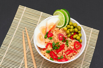 Beautiful Noodle Dish with Green Pea, Eggs, Red Hot Pepper, Greens and Lime with Chopsticks on Sushi Mat. Instant Noodles