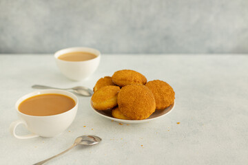 Delicious snack: two cups of black tea with milk and a plate of cookies on a gray background.