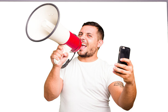 Young caucasian man holding megaphone in streaming with a phone isolated