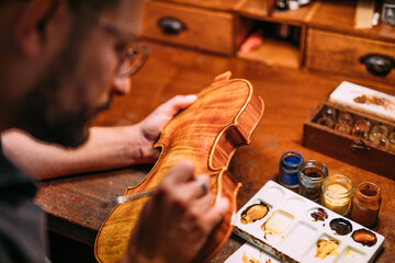Focused luthier varnishing violin in workshop