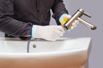 A plumber installs a faucet in a bathroom, connects a hose to the faucet, close-up