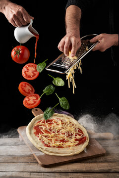 Crop chefs cooking pizza with tomatoes in dark studio