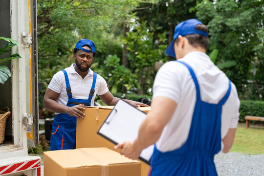 Man mover worker in blue uniform checking lists on clipboard while unloading cardboard boxes from truck.Professional delivery and moving service.