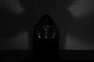 Hacker in black mask and hood at the table