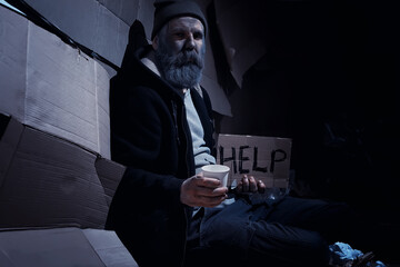 A homeless bearded man sits on boxes on the street and asks for help. Need a homeless person asks for money for food and overnight.