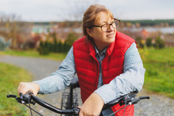 Fototapeta premium Middle aged smiling mature woman holdingt a bike with her hands on the grass on a green field. Summer or Autumn Country Vacation and Adventure Concept