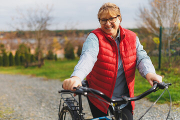 Middle aged smiling mature woman holdingt a bike with her hands on the grass on a green field. Summer or Autumn Country Vacation and Adventure Concept