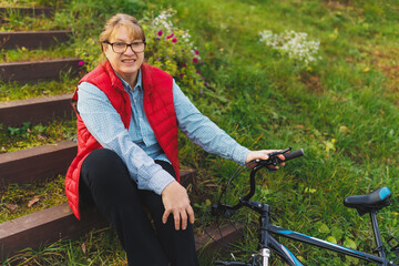 Fototapeta premium Middle aged smiling mature woman holdingt a bike with her hands on the grass on a green field. Summer or Autumn Country Vacation and Adventure Concept