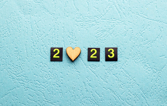 happy 2023 year.small digits numbers in square magnetic shapes on blue structure paper or instead of car temporary parking card phone holder.2022 in mini trash bin can isolated in black.wooden heart