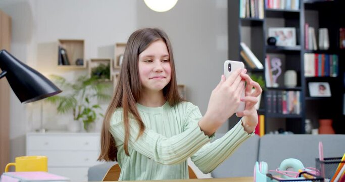 Happy girl making selfies, chatting with friends sitting in room. Using phone online. Female teenager taking pictures of herself on iPhone to post and speak with people in Internet. Internet concept