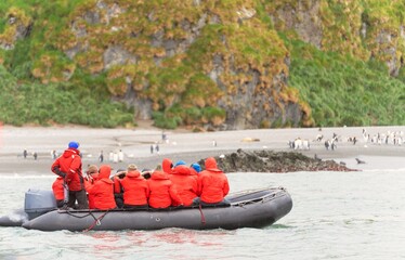 ein Zodiac / Schlauchboot mit Antarktis Touristen in roten Parkas beobachtet Pinguine an der Küste von Südgeorgien