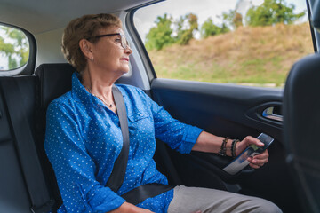 Beautiful happy senior woman in a blue blouse in the passenger seat in a car enjoying a trip - obrazy, fototapety, plakaty